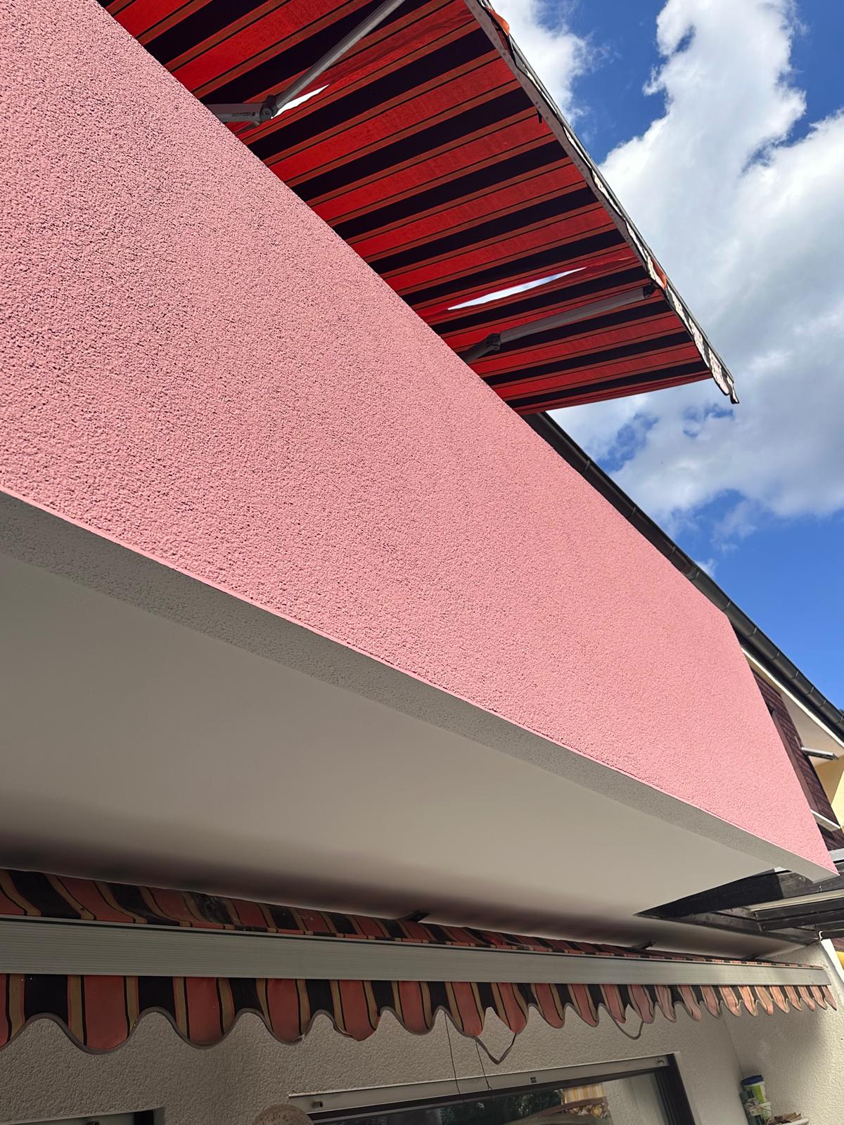 Fassadendetail in kräftigem Rosé mit Markise vor blauem Himmel